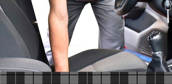 Homme penché vers le siège avant d’un véhicule avec intérieur gris
