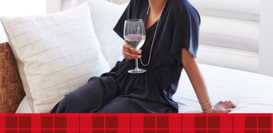 Woman with a glass of white wine sitting on a white couch 
